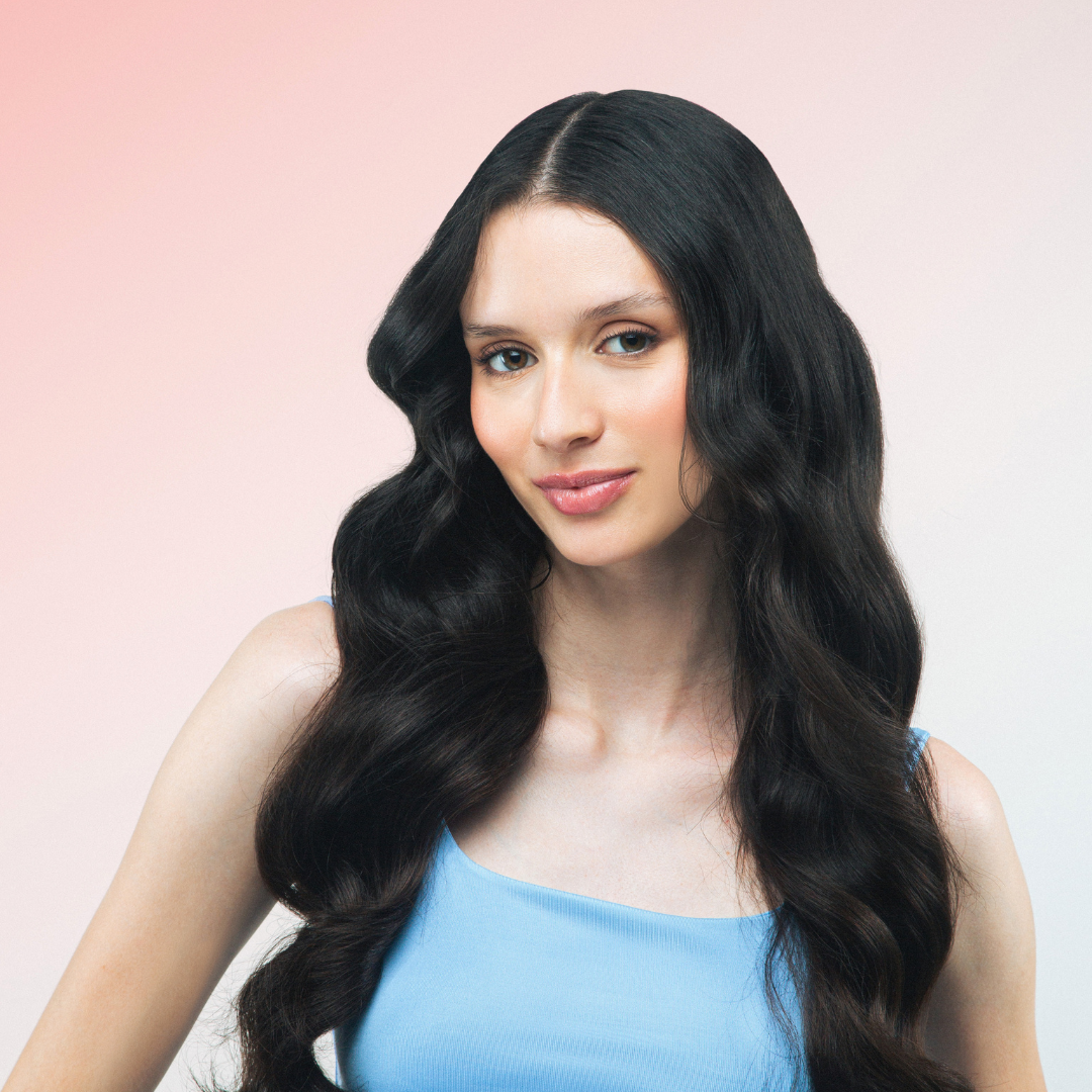 Woman with long, wavy hair wearing a blue top against a pink background