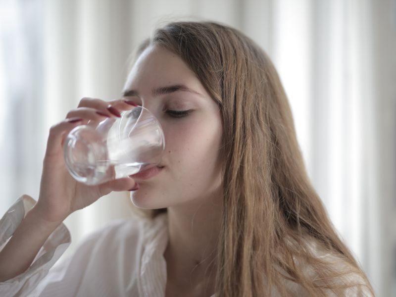 A woman drinking water to hydrate her hair