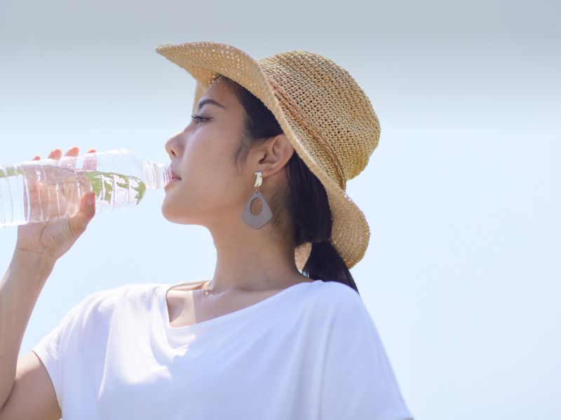 A woman drinking water and wearing a hat