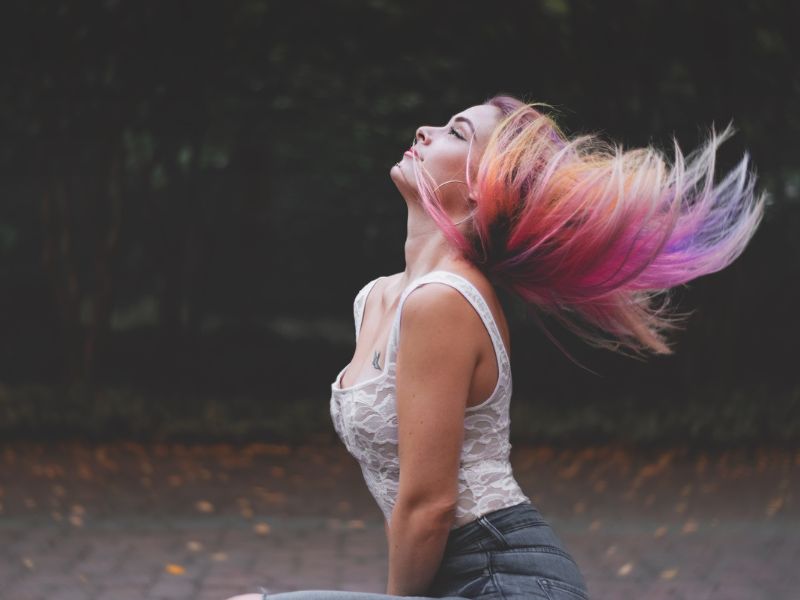 A sideview of a woman with colored hair, waving her hair