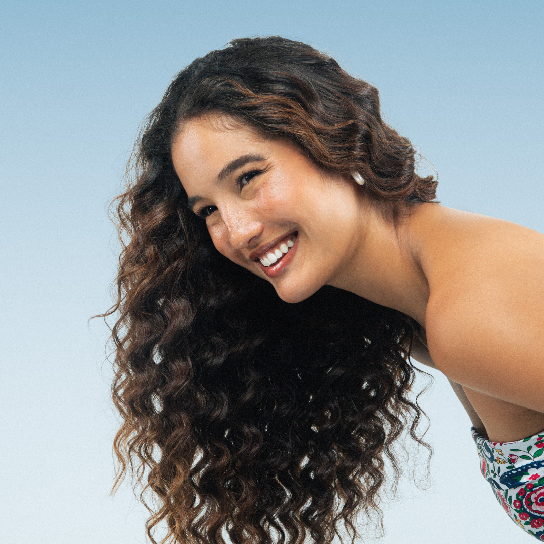 Woman with curly hair smiling against a light blue background