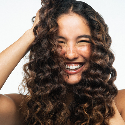 Woman with curly hair smiling against a plain background