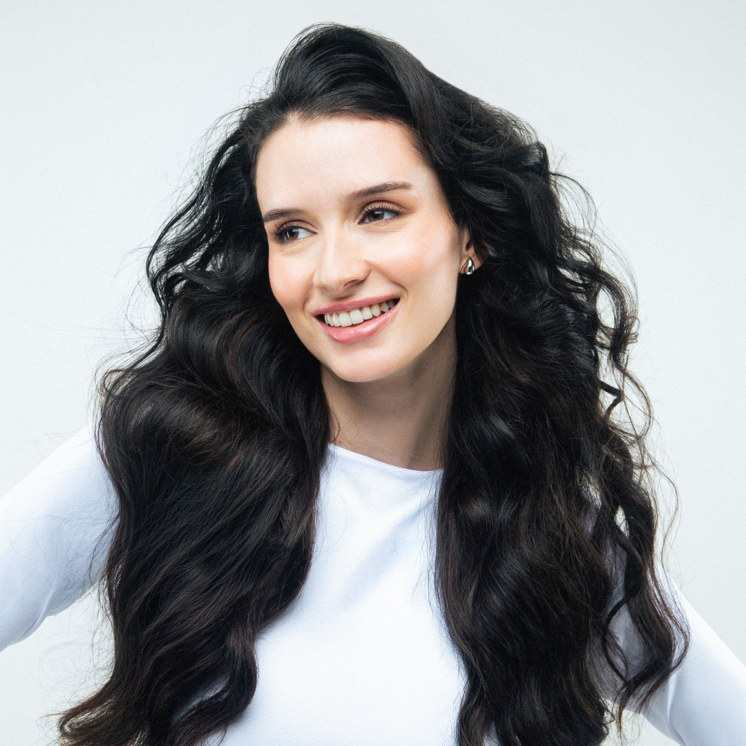 Woman with long, wavy black hair smiling against a light background
