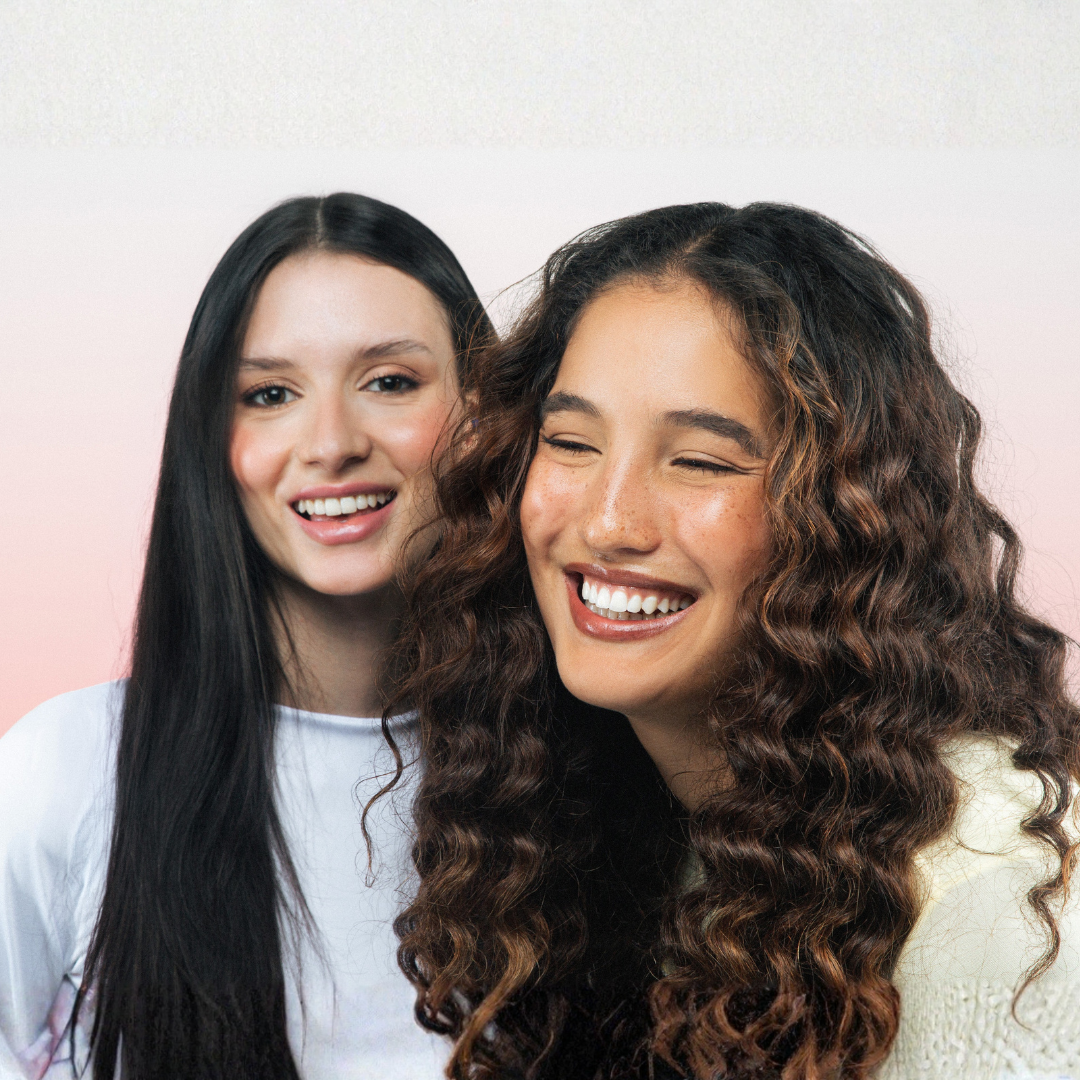 Two women smiling and posing together against a light pink background